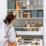 a woman reaching for a jar in front of a pantry shelf full of food storage items from glass jars to tins