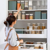 a woman reaching for a jar in front of a pantry shelf full of food storage items from glass jars to tins