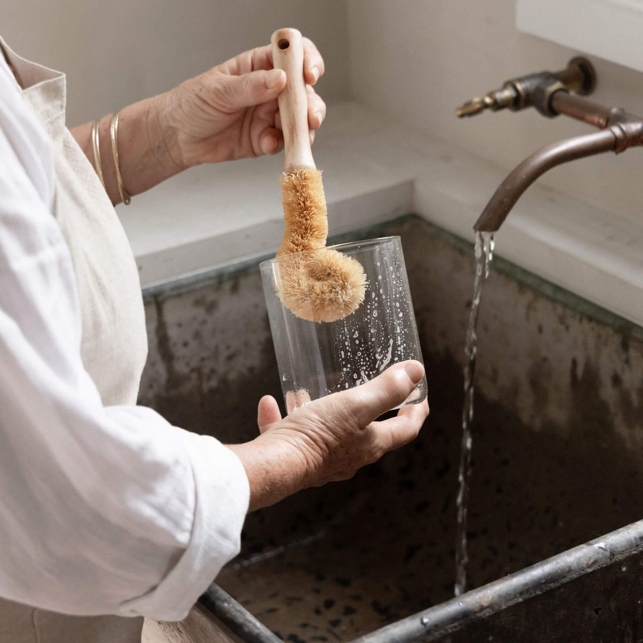 Tallow Rectangle glass pantry jar being scrubbed clean next to running water at a kitchen sink, demonstrating hand-wash ease — lid removed.