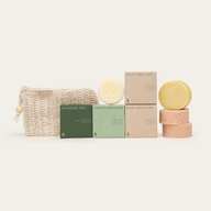 a shampoo, conditioner and 2 body wash round chunks next to their green and beige plastic-free packaging including a cleaning body soap bag