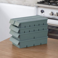 Four eucalyptus green Seed & Sprout silicone freezer trays stacked neatly on a wooden surface, showing the interlocking stackable design with lids secured