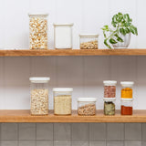 A shelf with square pantry jars and square spice containers on it. The jars contain popcorn, flour, grain, oats and spices