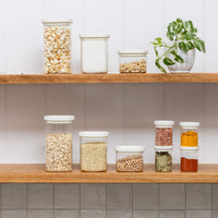 A shelf with square pantry jars and square spice containers on it. The jars contain popcorn, flour, grain, oats and spices